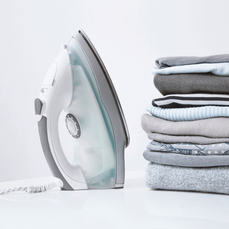 Iron on a white background next to a pile of folded clothes.