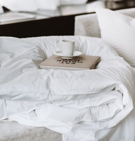 White hotel duvet folded, on top of it their is a book and a cup of coffee.