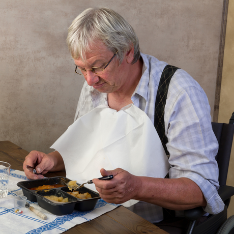 Senior man eating at a table, wearing a white bibs