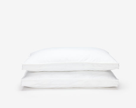 Two white hotel pillows, one on top of the other in a pile.